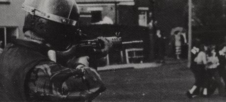 Photo of cop shooting plastic bullets at a crowd of cowering children